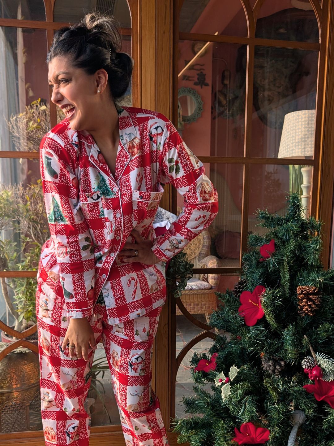 Woman wearing a red and white patterned pajama set standing in front of a decorated Christmas tree.