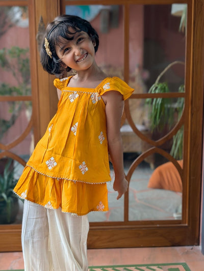 girl wearing a bright yellow festive indian kurti top with white floral patterns getting ready for diwali