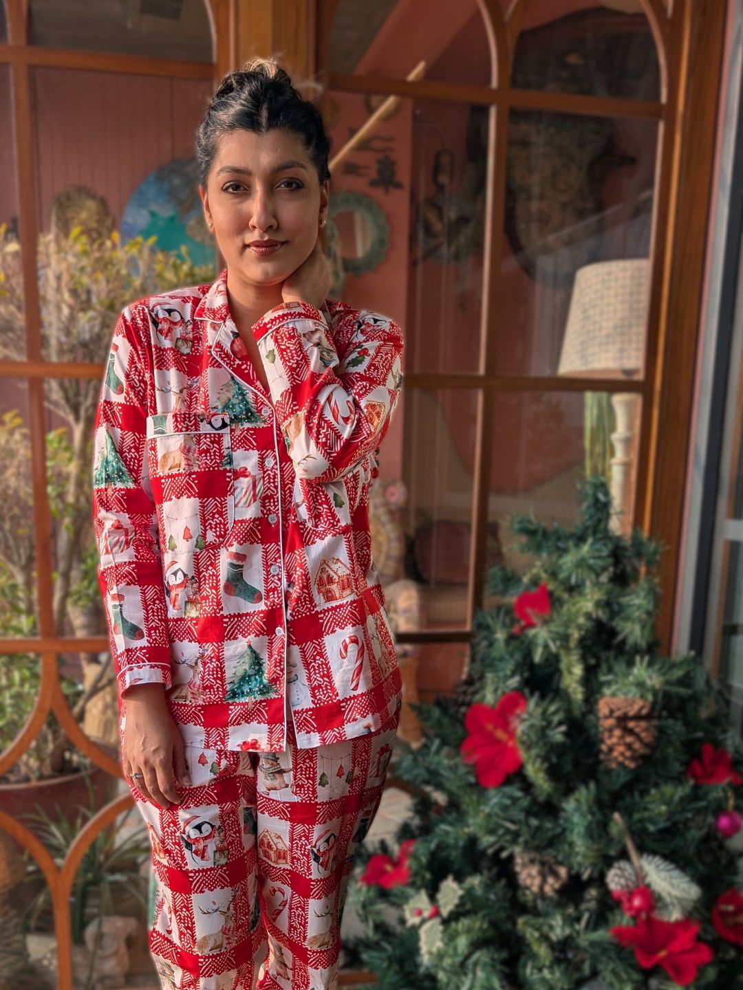 Person wearing a red and white chequered night suit pajama set standing in front of a decorated Christmas tree.