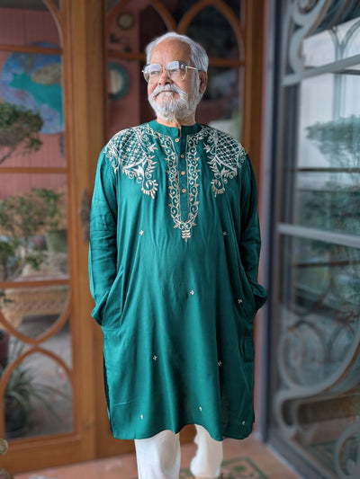 Man wearing a green embroidered kurta standing in front of a decorative door.