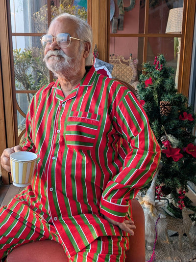 Man wearing red and green striped pajamas sitting in a room decorated for Christmas.