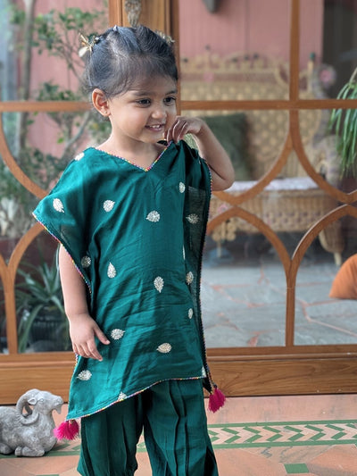 Girl wearing a green ethnic outfit with white embroidery and pink tassels. 