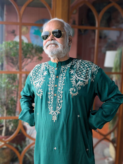 Stylish man wearing a green embroidered made in india kurta with sunglasses in front of a decorative wall.