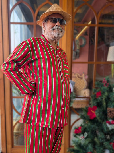 Man wearing a red and green pinstriped night suit pajama set with a straw hat in front of a decorated Christmas tree.