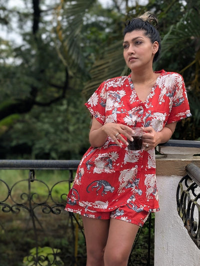 Woman in a red floral no bra needed night dress standing outdoors with greenery in the background