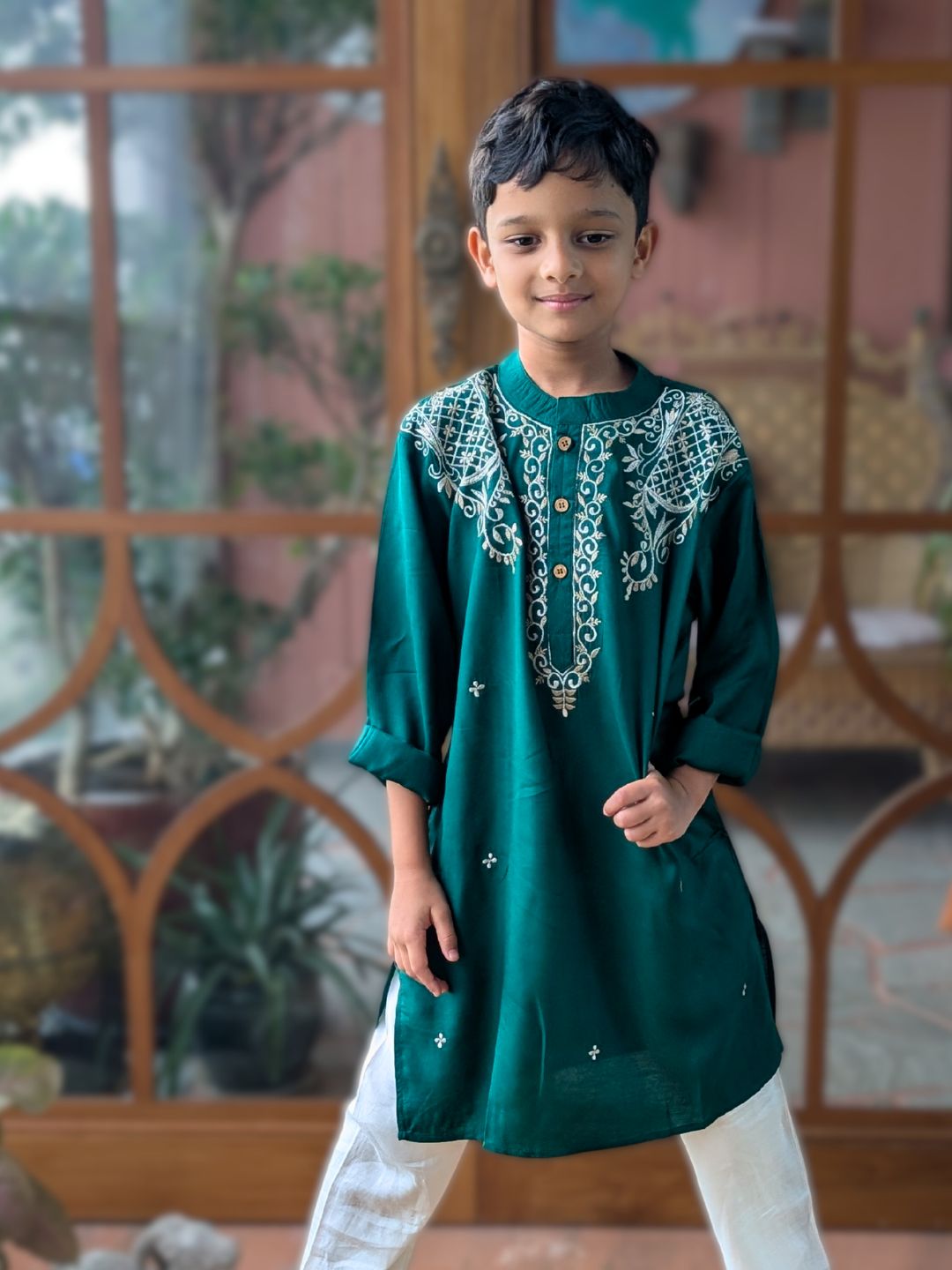 Child wearing a green embroidered kurta with white pants in a decorative indoor setting.
