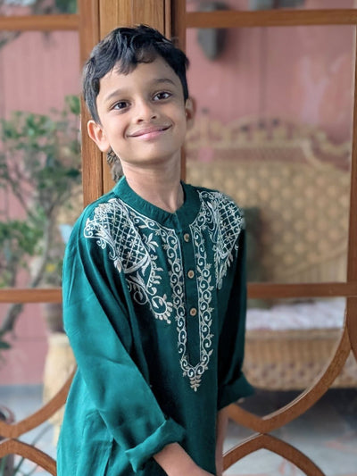 Child wearing a green embroidered traditional outfit sitting outdoors.