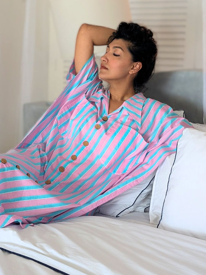 Person wearing a pink and blue striped front open button down nightdress lying on a bed.