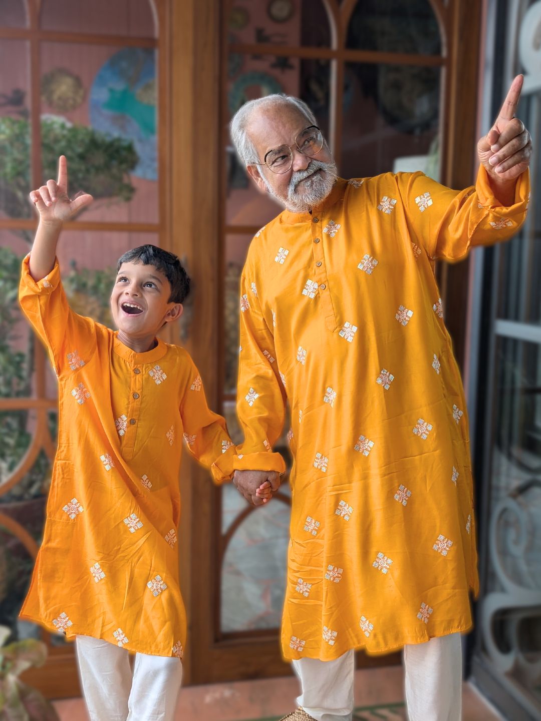 Man and child in matching twinning yellow kurtas standing in front of a decorative door.