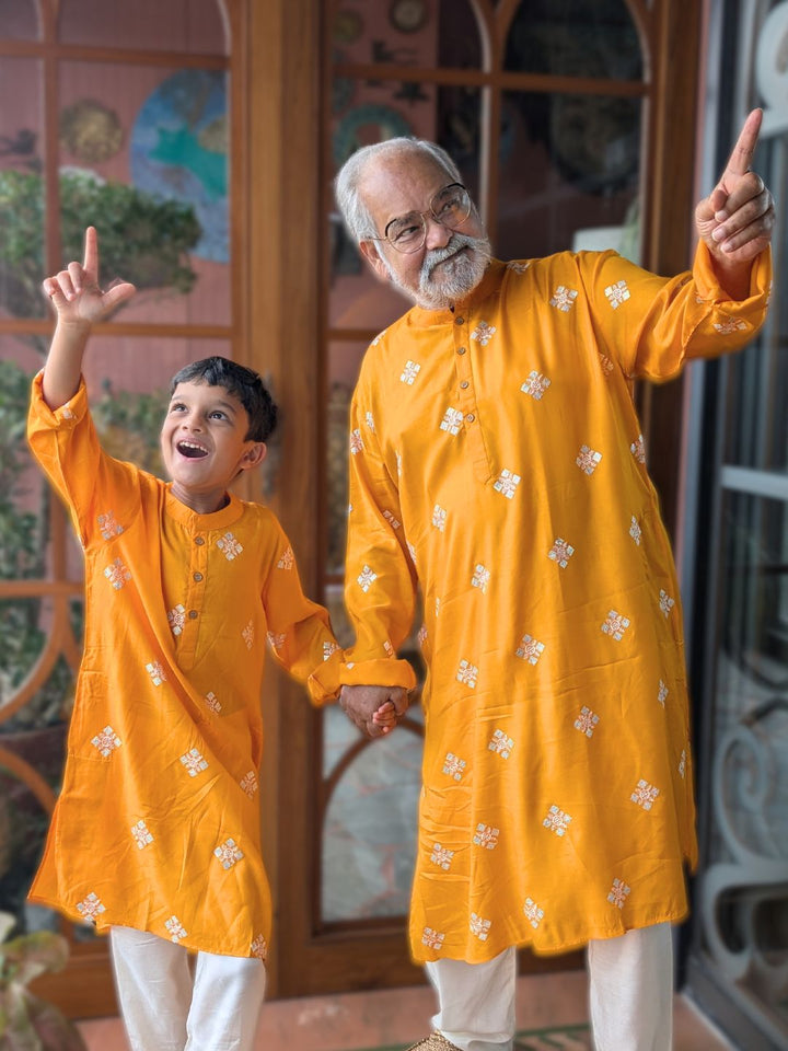 Man and child in matching twinning yellow kurtas standing in front of a decorative door.