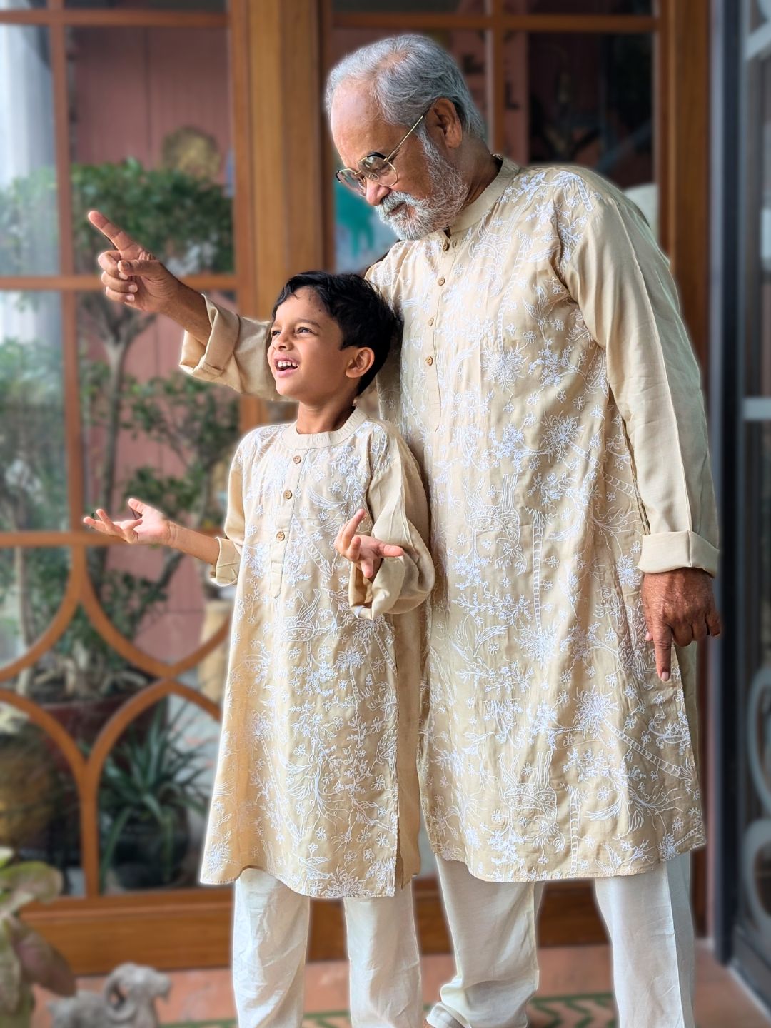 Man and child in matching traditional outfits standing together indoors.