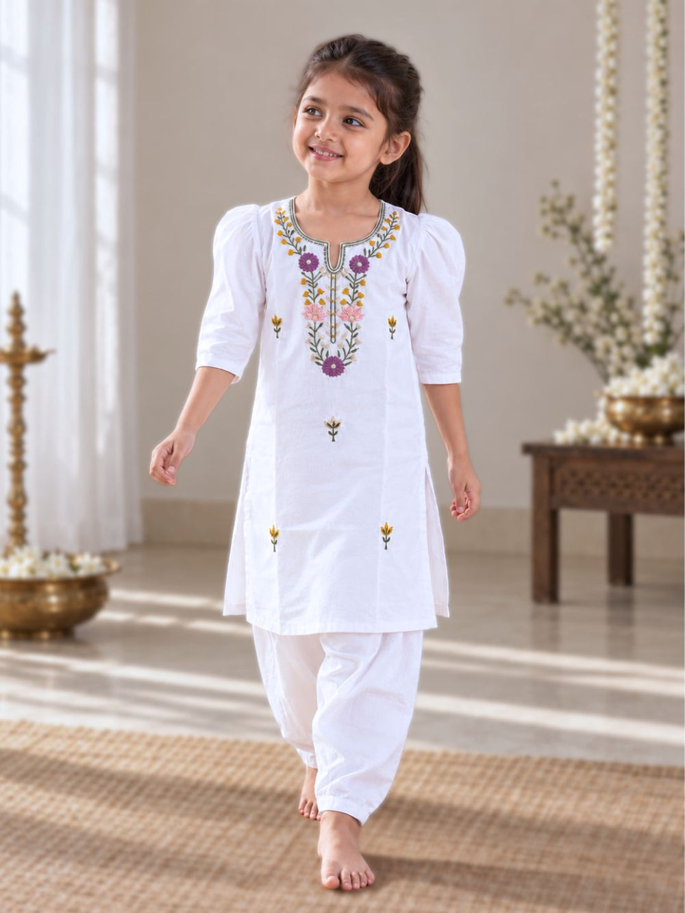 White cotton mulmul kurta for girls with pink, purple and mustard floral embroidery around the neckline
