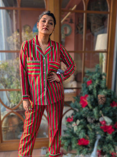 woman wearing red and green striped pajamas standing in a room with a Christmas tree.
