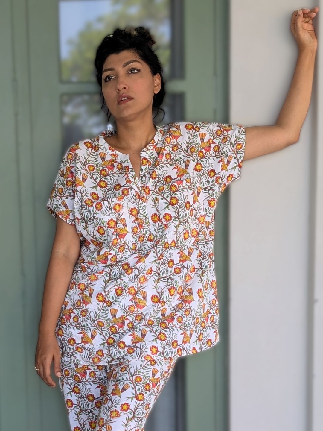 Woman wearing a floral no bra night pajama set leaning against a wall.
