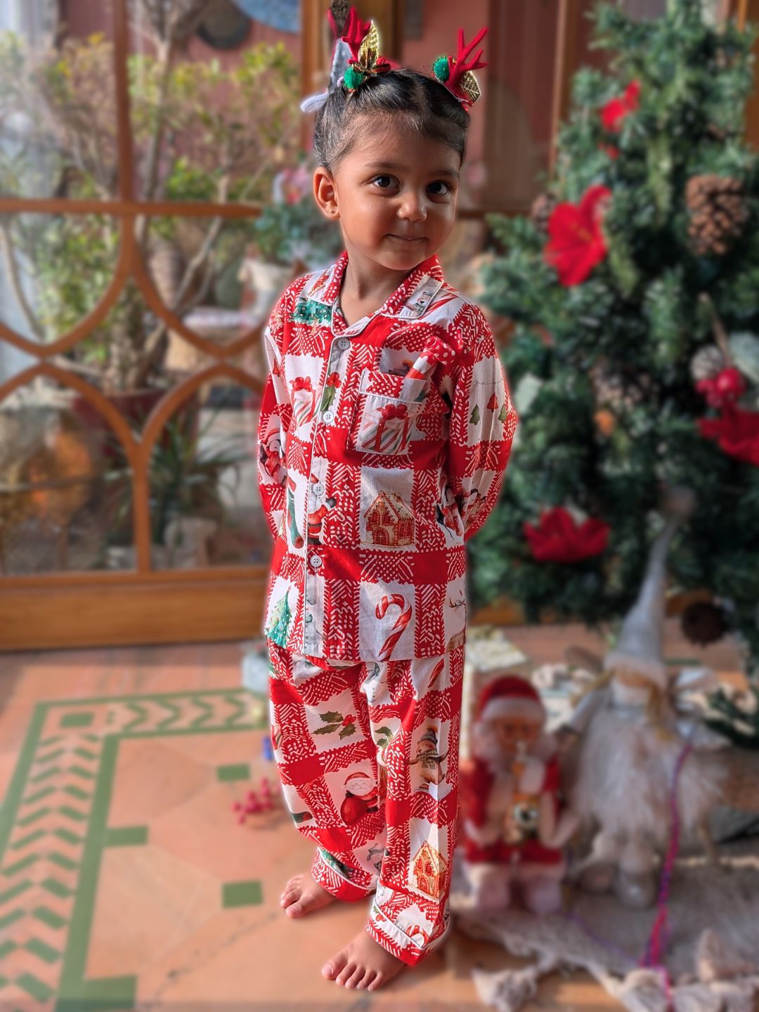 little girl wearing red and white Christmas-themed pajamas with a decorated tree in the background.