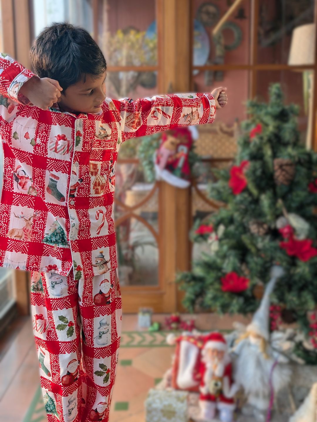 boy wearing a red and white Christmas-themed chequed pajama by an xmas tree