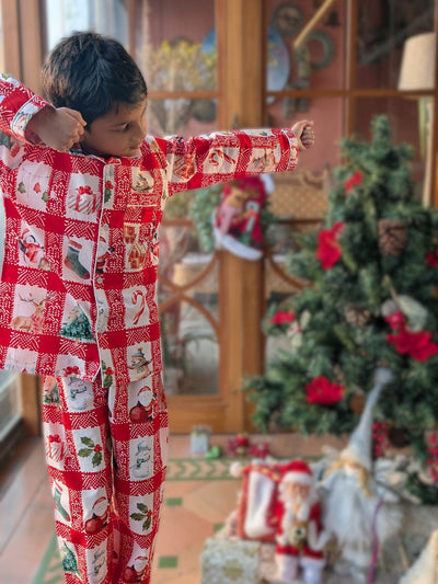 boy wearing a red and white Christmas-themed chequed pajama by an xmas tree