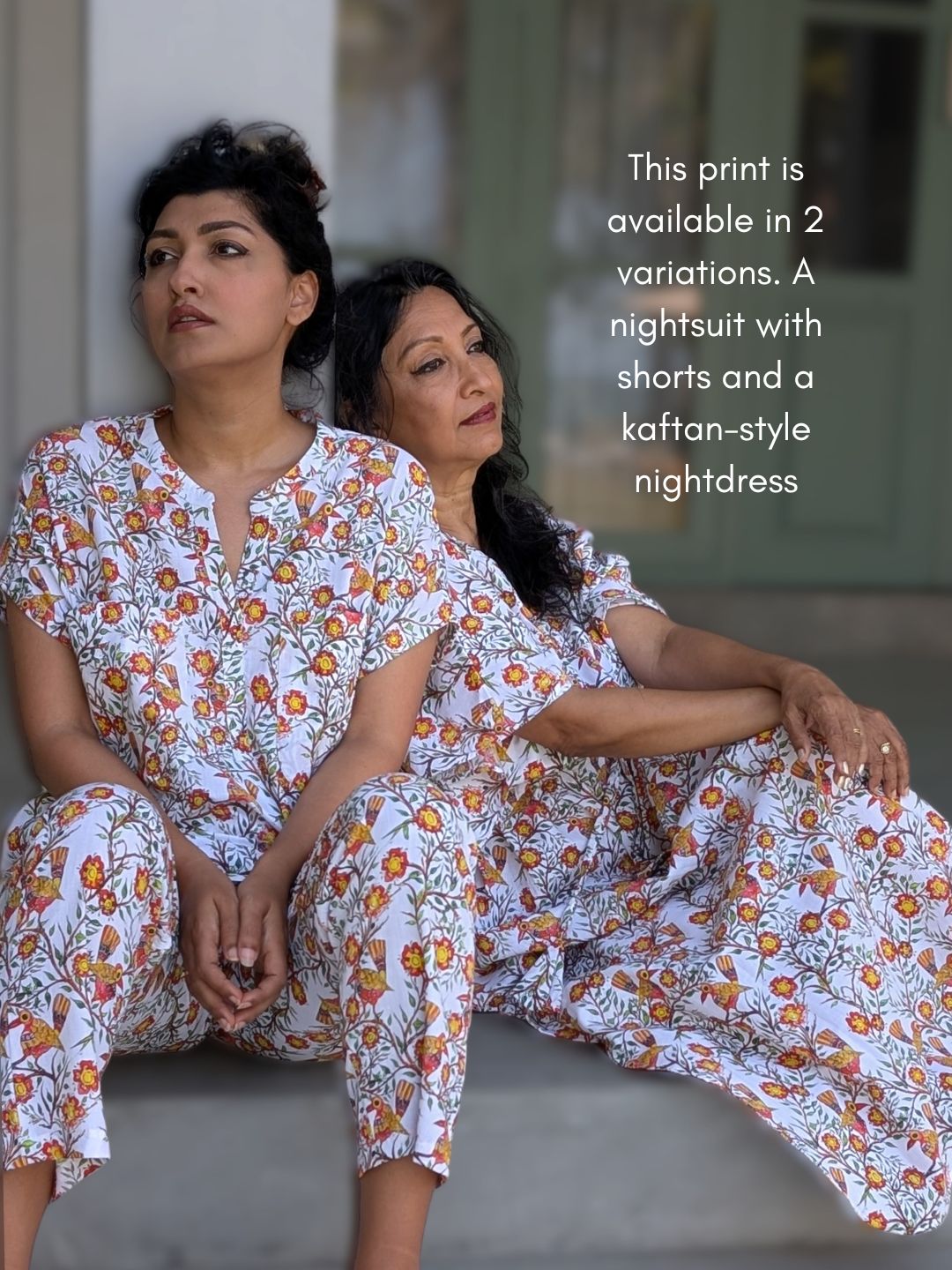 Two women wearing matching cotton floral nightwear sitting on a couch.