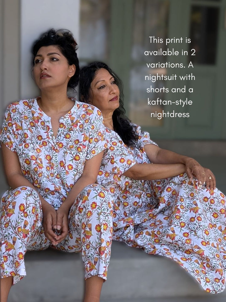 Two women wearing matching cotton floral nightwear sitting on a couch.