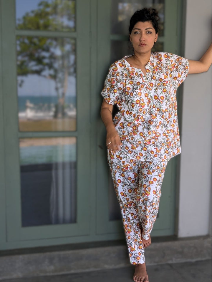 Woman wearing a floral pajama set standing in front of a glass door with a blurred outdoor view.