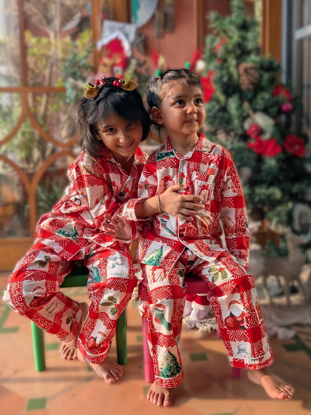 Two children in red Christmas-themed cotton pajamas sitting on a chair.