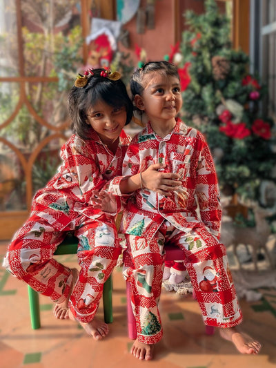 Two children in red Christmas-themed cotton pajamas sitting on a chair.