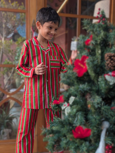 Child wearing red and green striped pajamas standing next to a decorated Christmas tree.