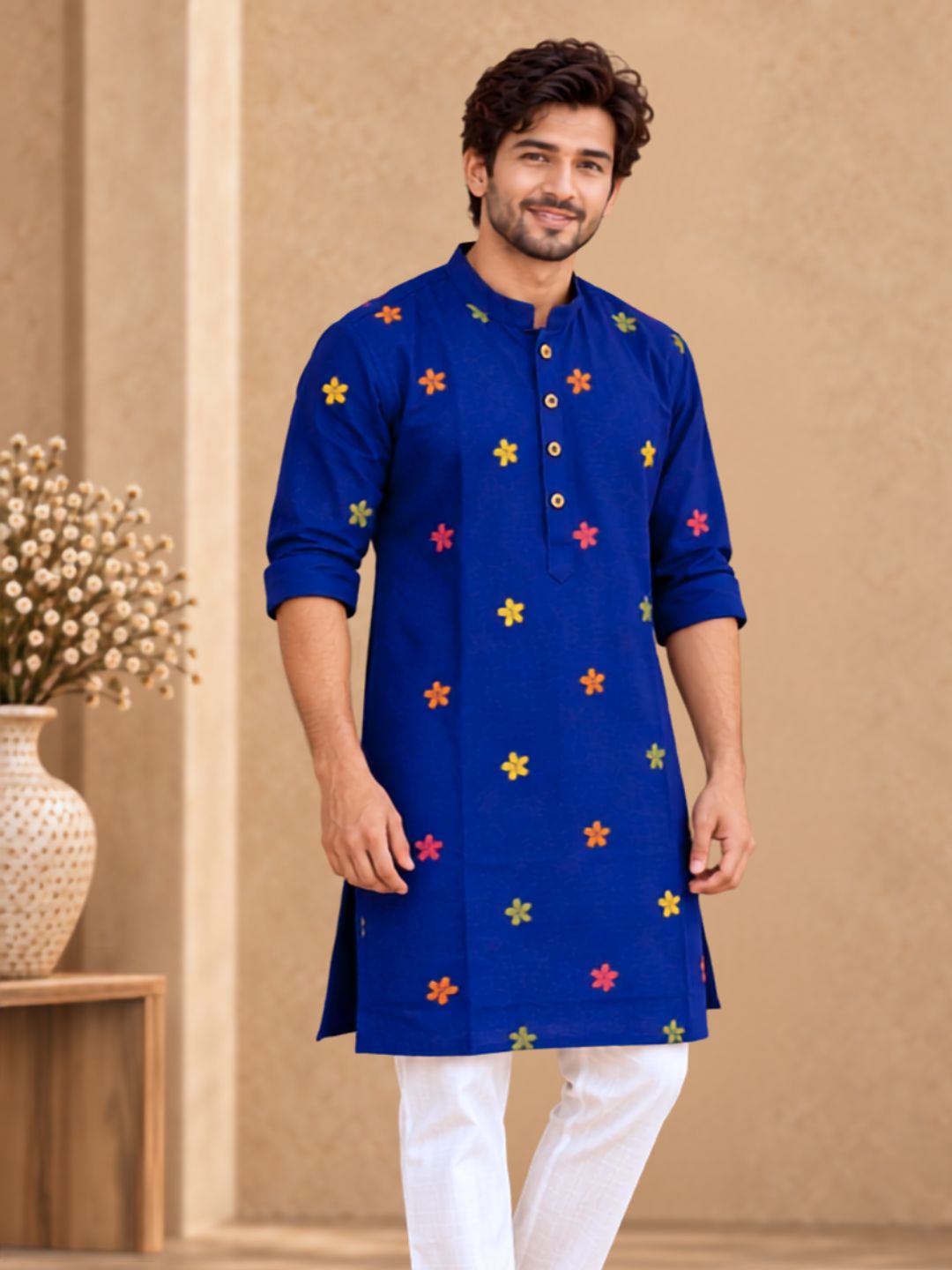 Man wearing a knee-length royal blue cotton kurta with colourful embroidered motifs, folded sleeves and white cotton pajamas.