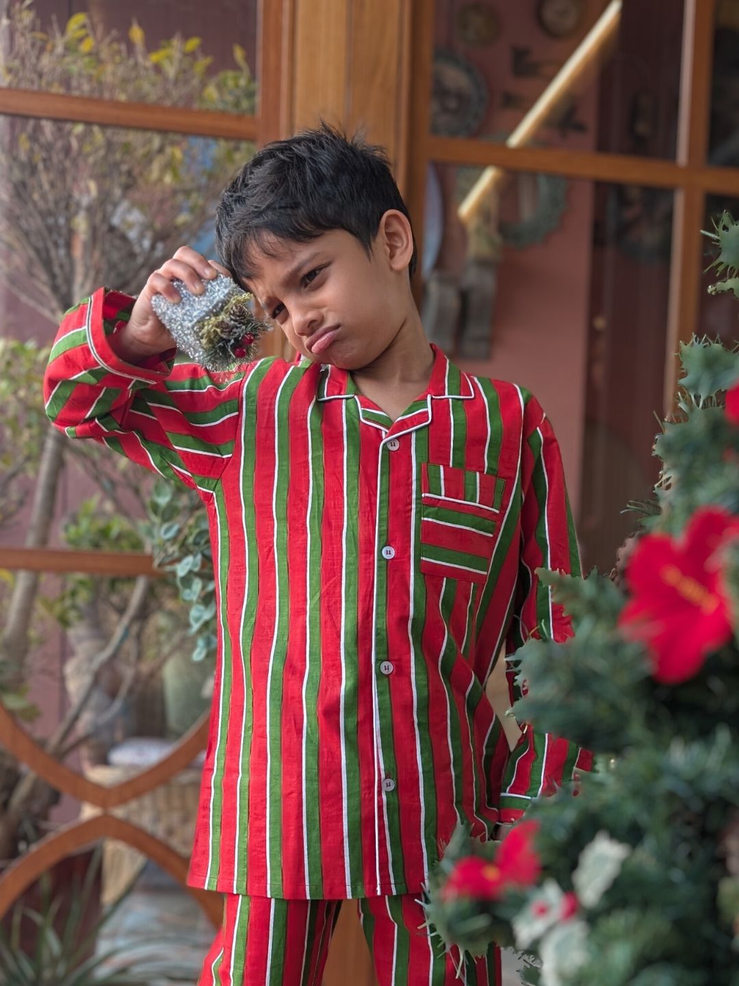 Child wearing red and green striped pajamas standing outdoors with plants in the background