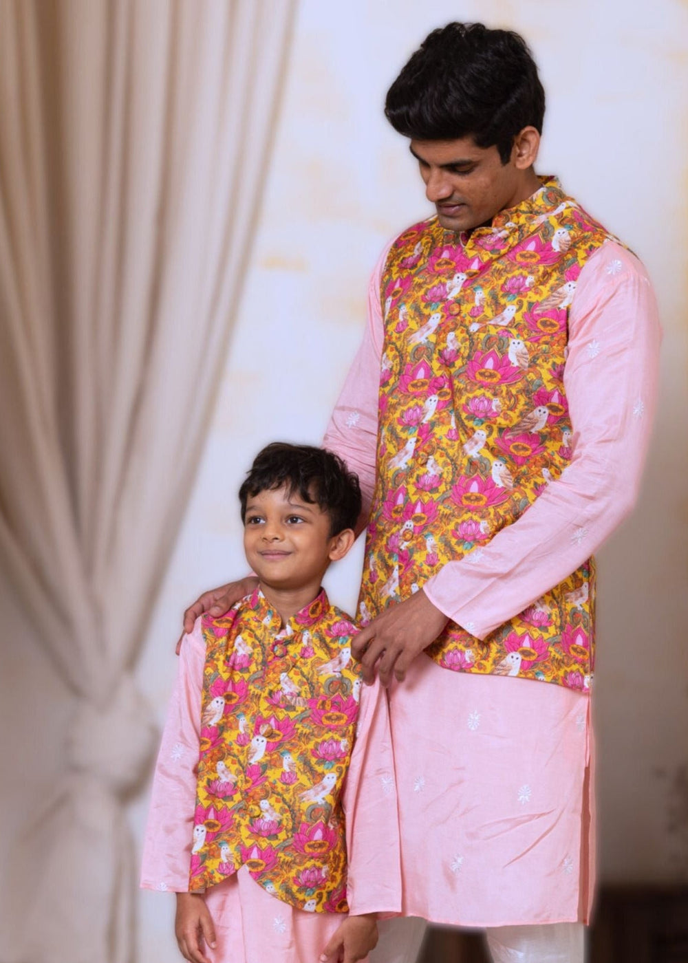 Man and child wearing matching traditional outfits with pink and yellow patterns.