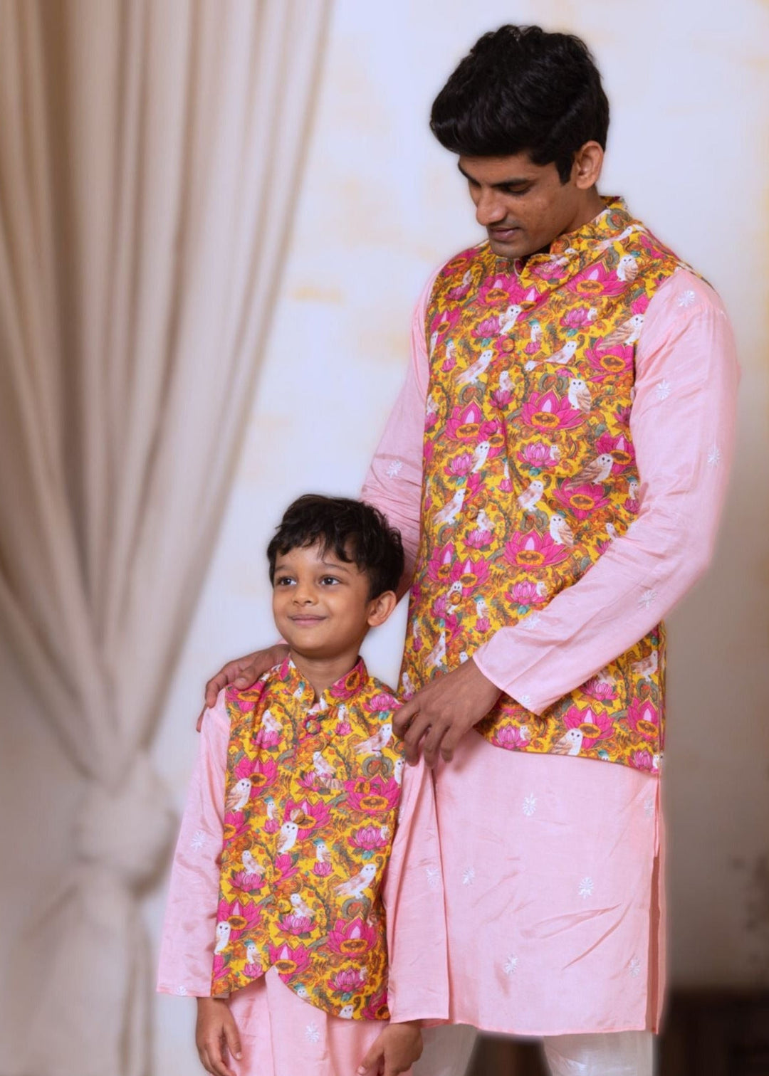 Man and child wearing matching traditional outfits with pink and yellow patterns.