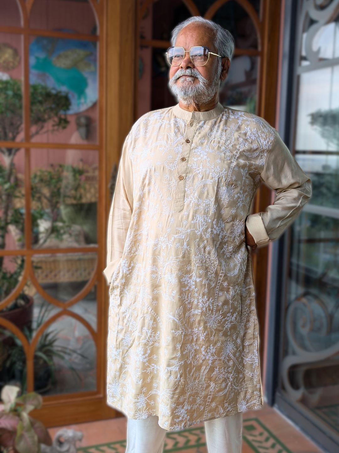 Man wearing a beige silk kurta with white embroidery in front of a decorative door.