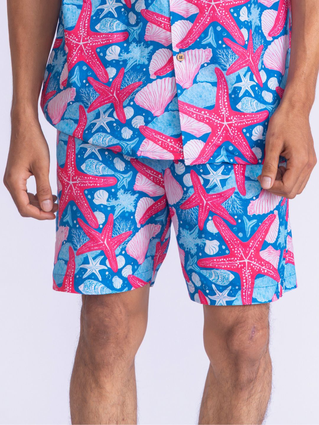 Person wearing a colorful swim shorts with starfish and shell pattern on a white background