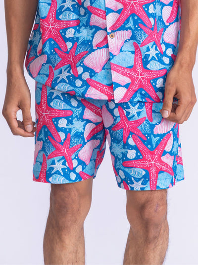 Person wearing a colorful swim shorts with starfish and shell pattern on a white background