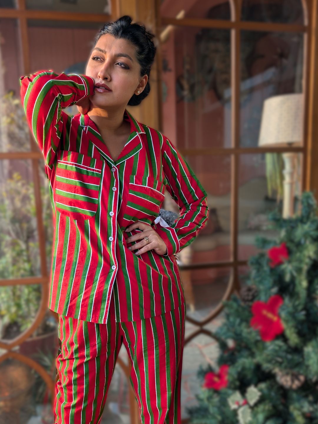 Person wearing red and green striped pajamas standing in front of a decorative window with plants.