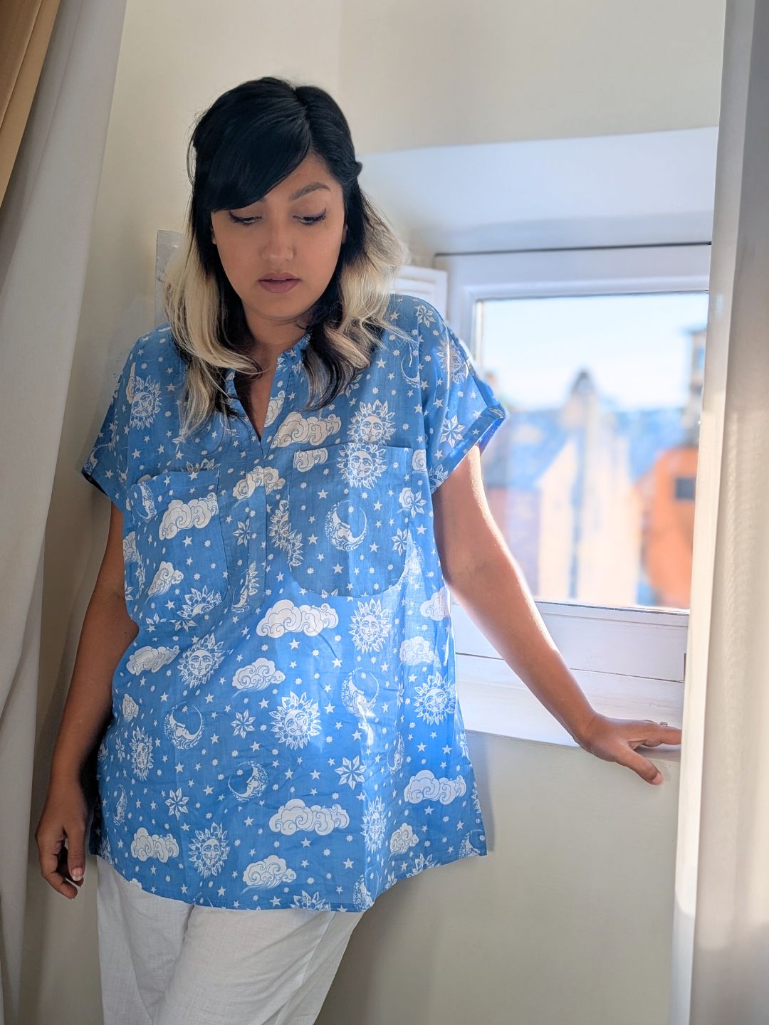 Person wearing a blue patterned cotton night suit standing indoors near a window.