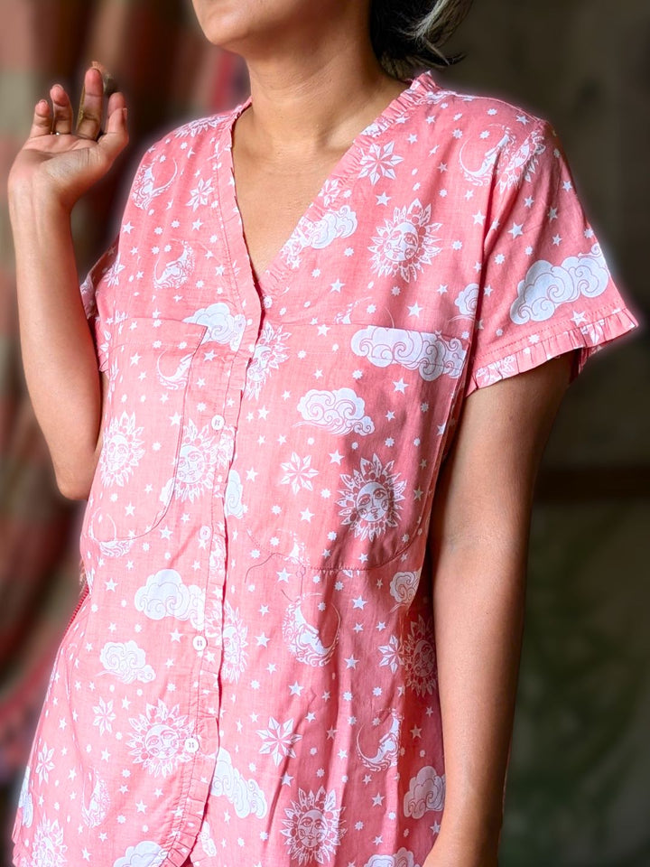 Person wearing a pink no bra nightsuit with pockets with white cloud patterns against a blurred background