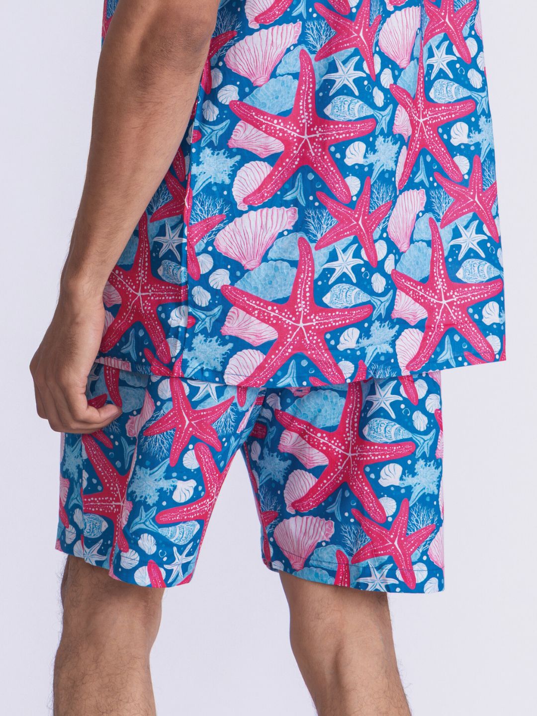 Person wearing blue shorts with starfish and shell design on a white background