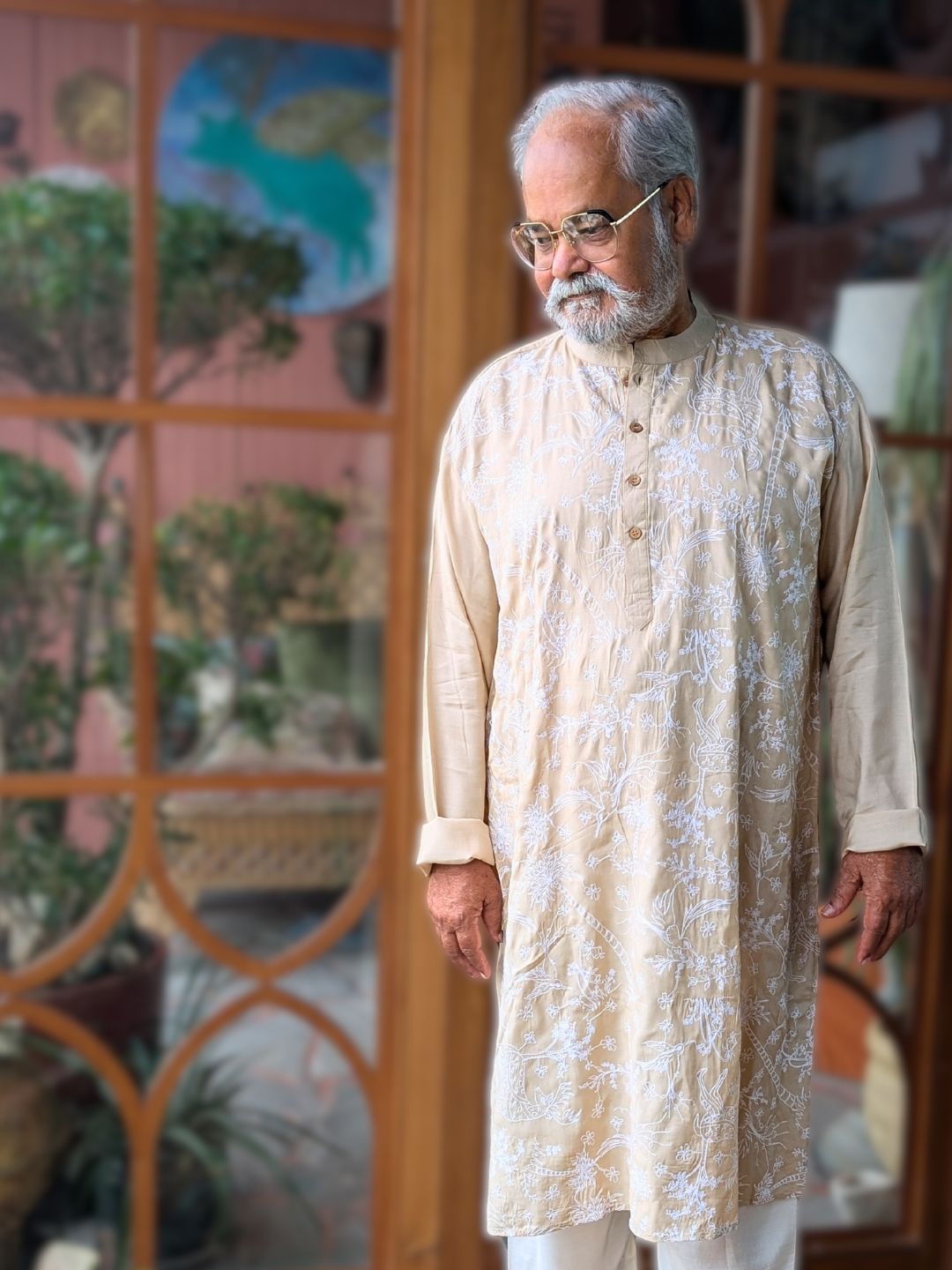Man wearing a cream off white kurta with white embroidery in a decorative indoor setting