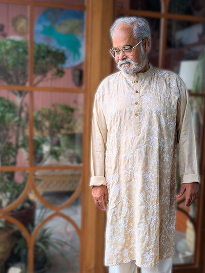 Man wearing a cream off white kurta with white embroidery in a decorative indoor setting