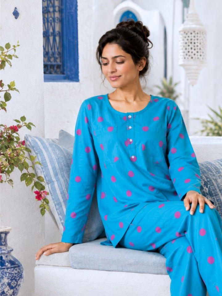 A woman wearing a bright blue long-sleeve pajama set with pink polka dots. the pajama has no bra or braless pockets on the chest for extra comfort