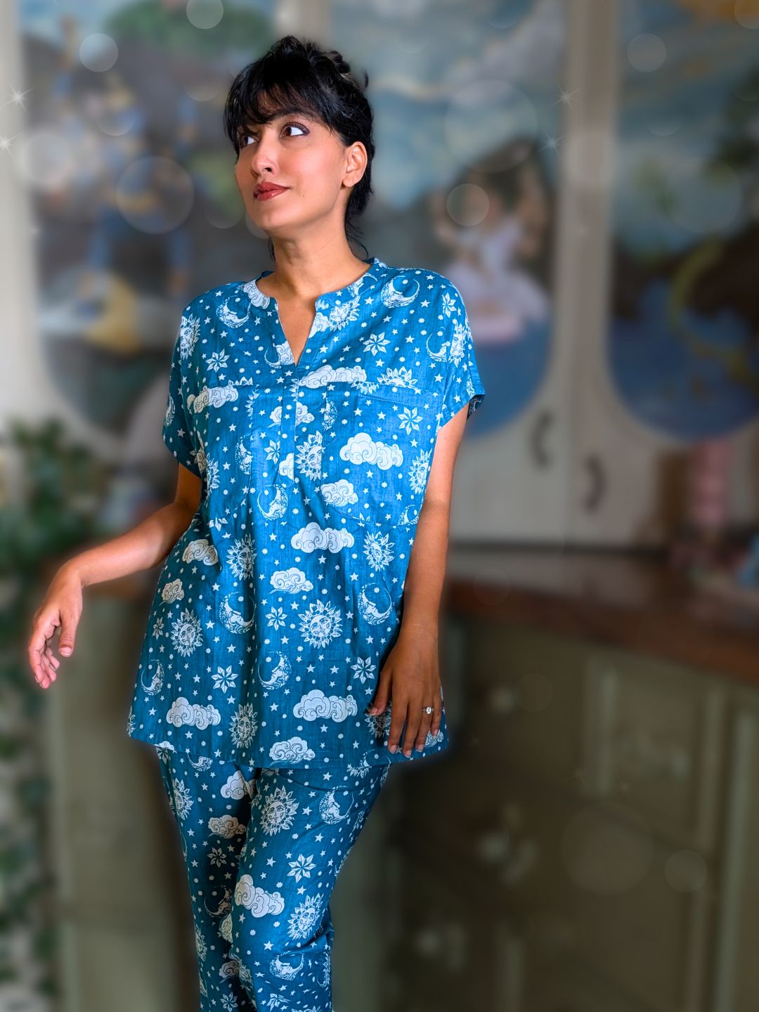 Woman wearing a blue no bra cotton pajama set with cloud patterns in front of a decorative wall.