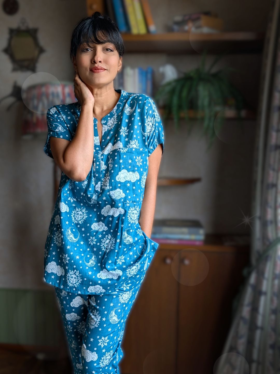 Woman looking comfortable and lounging in a a blue coord pajama set with cloud pattern in a room.