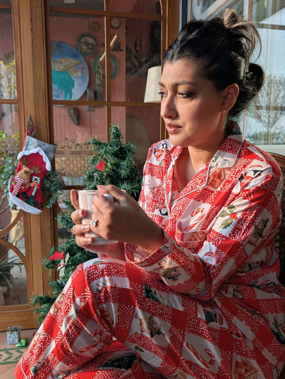 Woman in a festive red and white pajama set sitting by a Christmas tree.