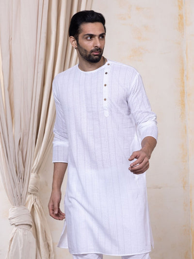 Man wearing a white self pattern kurta against a beige curtain background