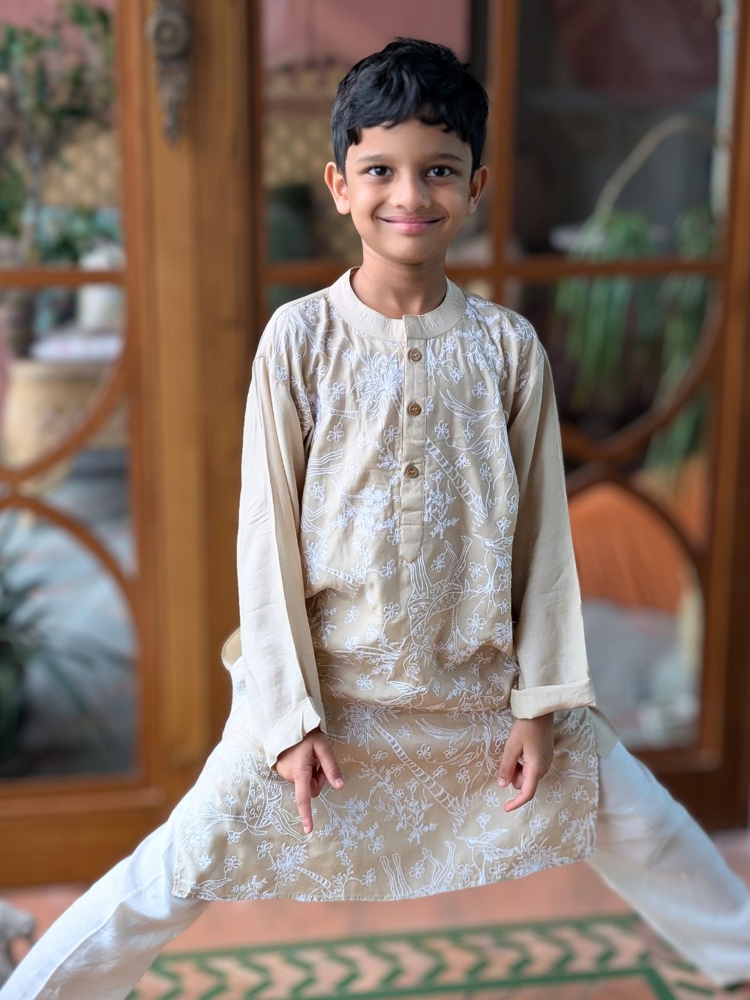 Young boy in traditional attire standing indoors with decorative elements in the background