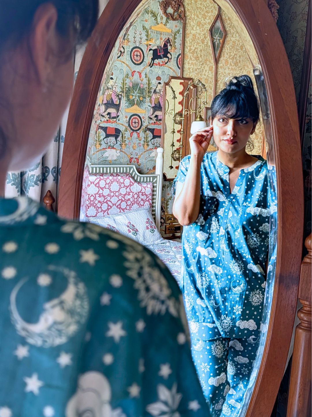 Woman in a blue patterned outfit standing in front of an ornate mirror.