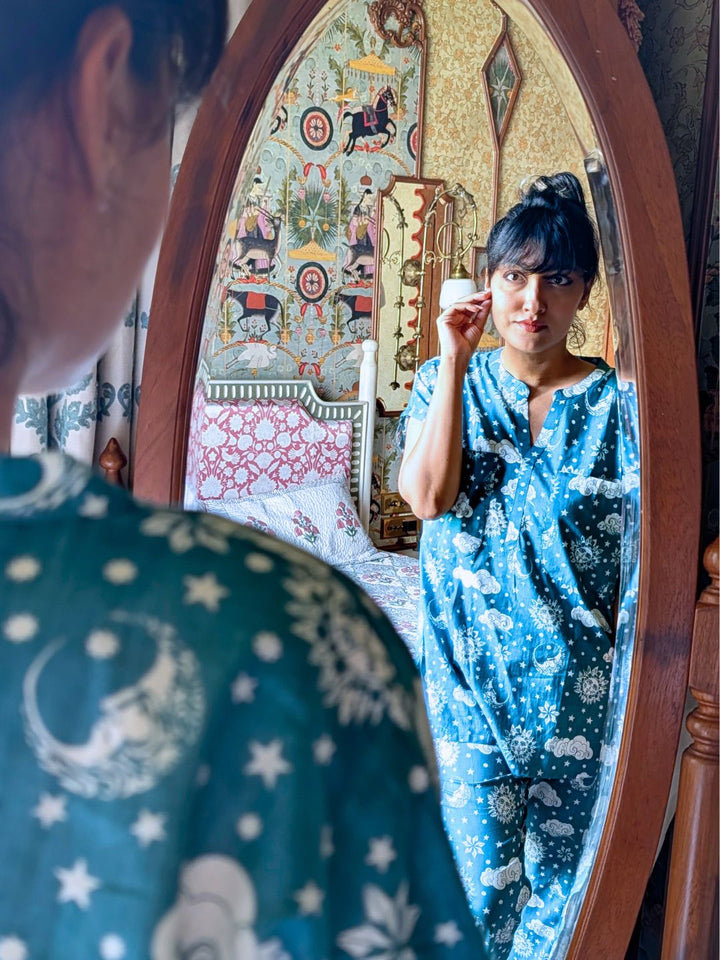 Woman in a blue patterned outfit standing in front of an ornate mirror.