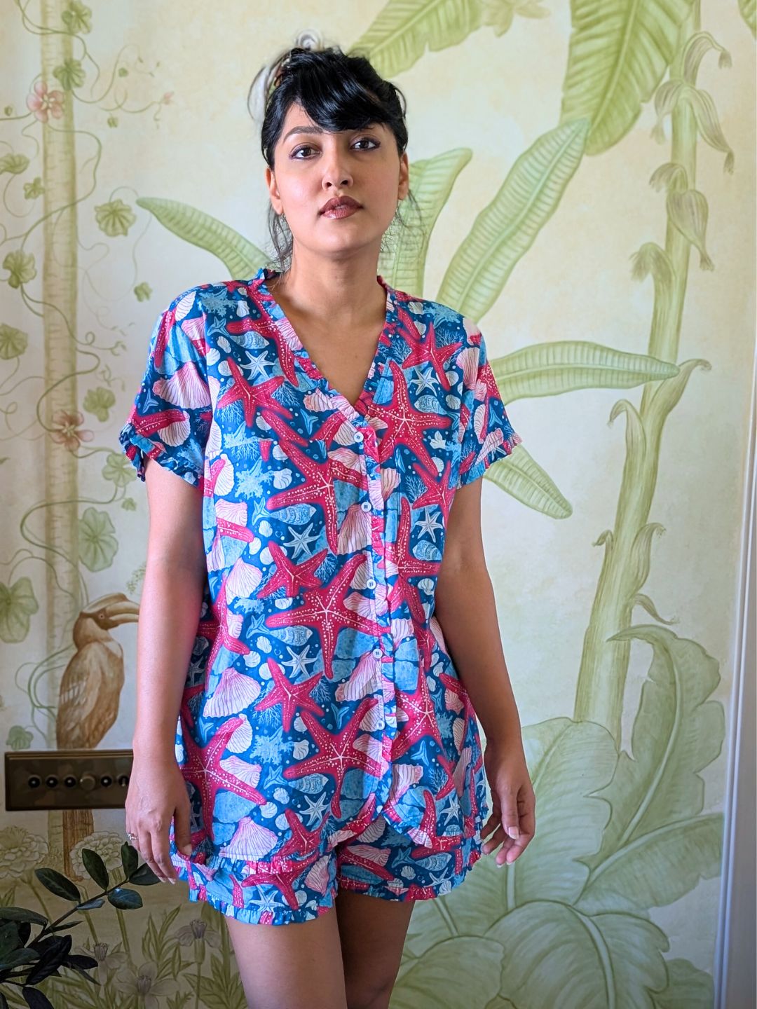 Woman wearing a colorful starfish-patterned nightsuit and loungewar against a floral wallpaper background