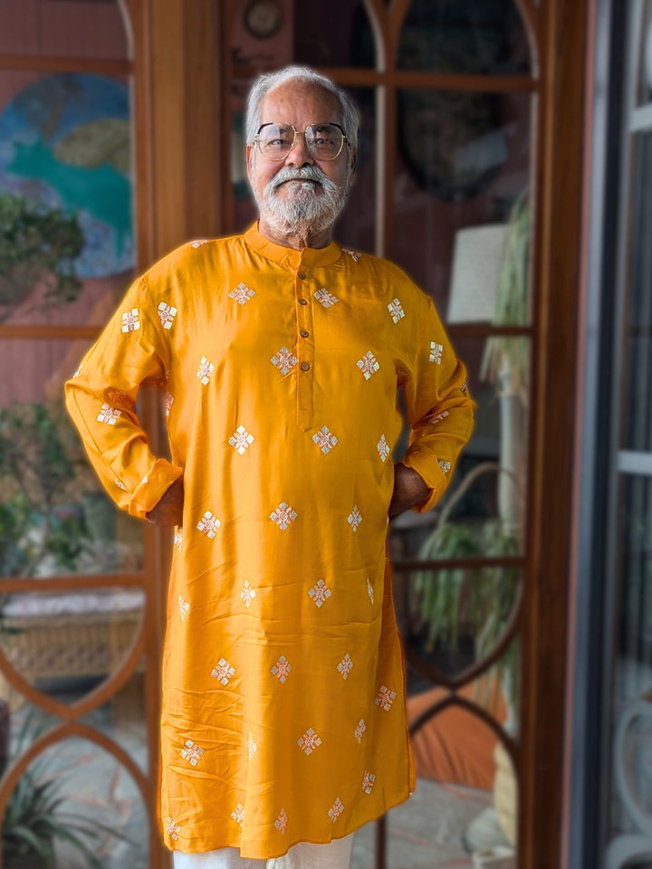 Man wearing a canary yellow silk kurta with white sequinned embroidery standing in a room with decorative elements.